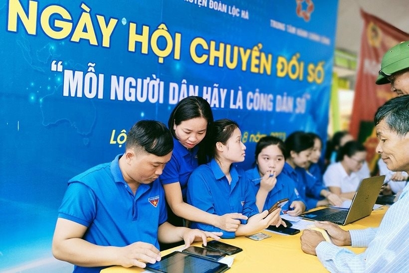 A group of people sitting at a table with laptops and tabletsDescription automatically generated