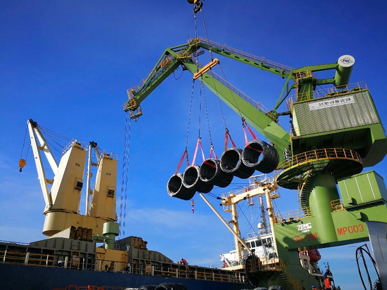 A crane lifting pipes from a craneDescription automatically generated